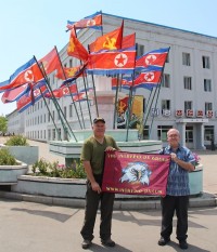 Members of the Intrepid DX group hold their banner next to a monument in the DPRK.