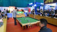 Image shows small robots on a table-sized football pitch. A person is standing nearby observing the robots.