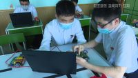 Two middle school students are seated looking at a laptop PC while examining a small robot
