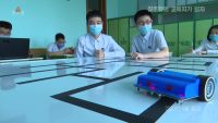 Two students look on while a small, two-wheeled robot follows a course marked out on a table top
